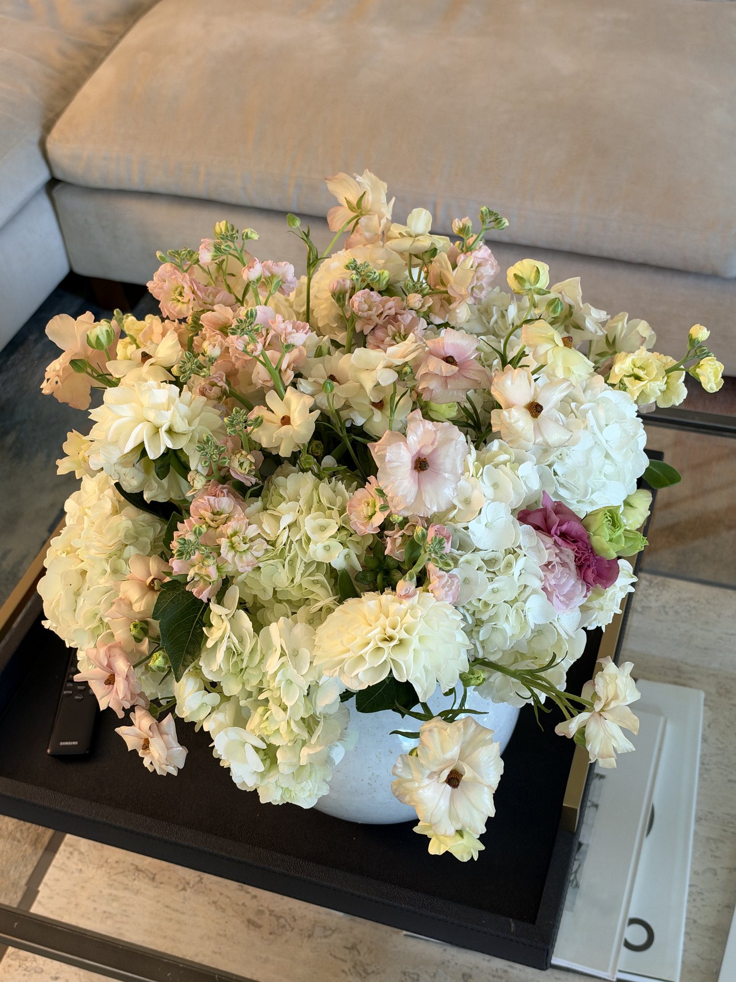 A large garden-style arrangement of blush stock, cream roses, and white hydrangea in a white bowl