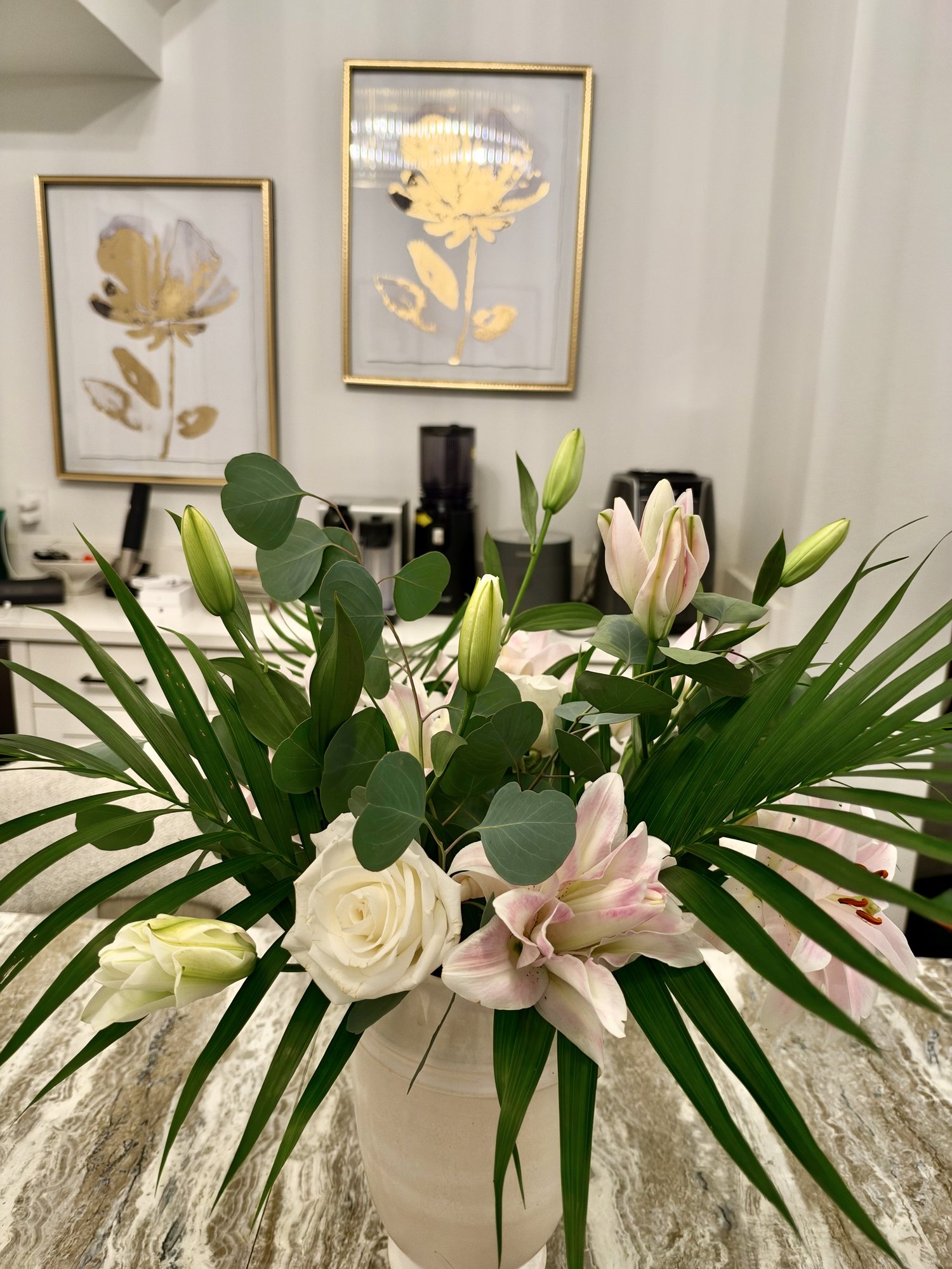 Pink lilies and white roses with palm fronds and eucalyptus in a white ceramic vase