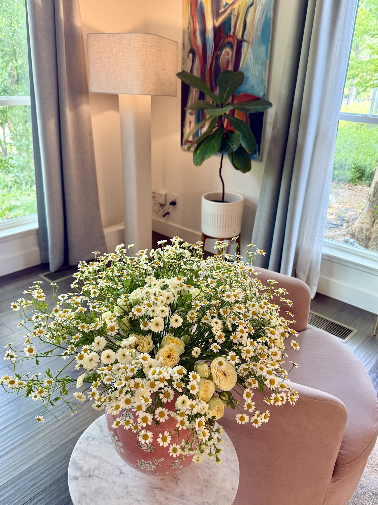 A generous arrangement of chamomile daisies and cream garden roses in a terracotta vase in a bright sitting area