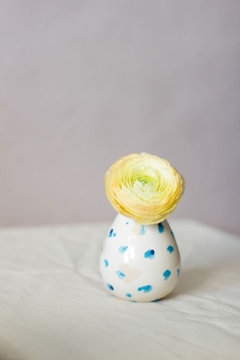 A single yellow ranunculus in a small white bud vase with blue spots